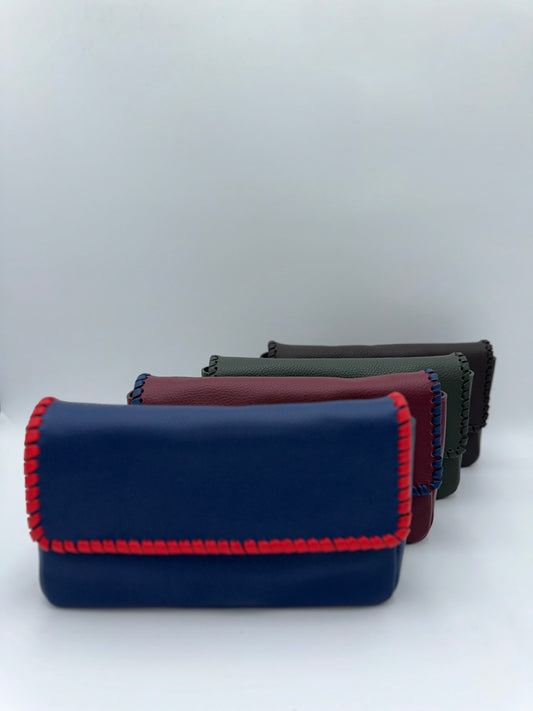 Four leather clutch wallets arranged in a row, featuring a prominent navy blue wallet in the foreground with red whipstitching, followed by burgundy, dark green, and dark brown wallets, all on a light gray background.