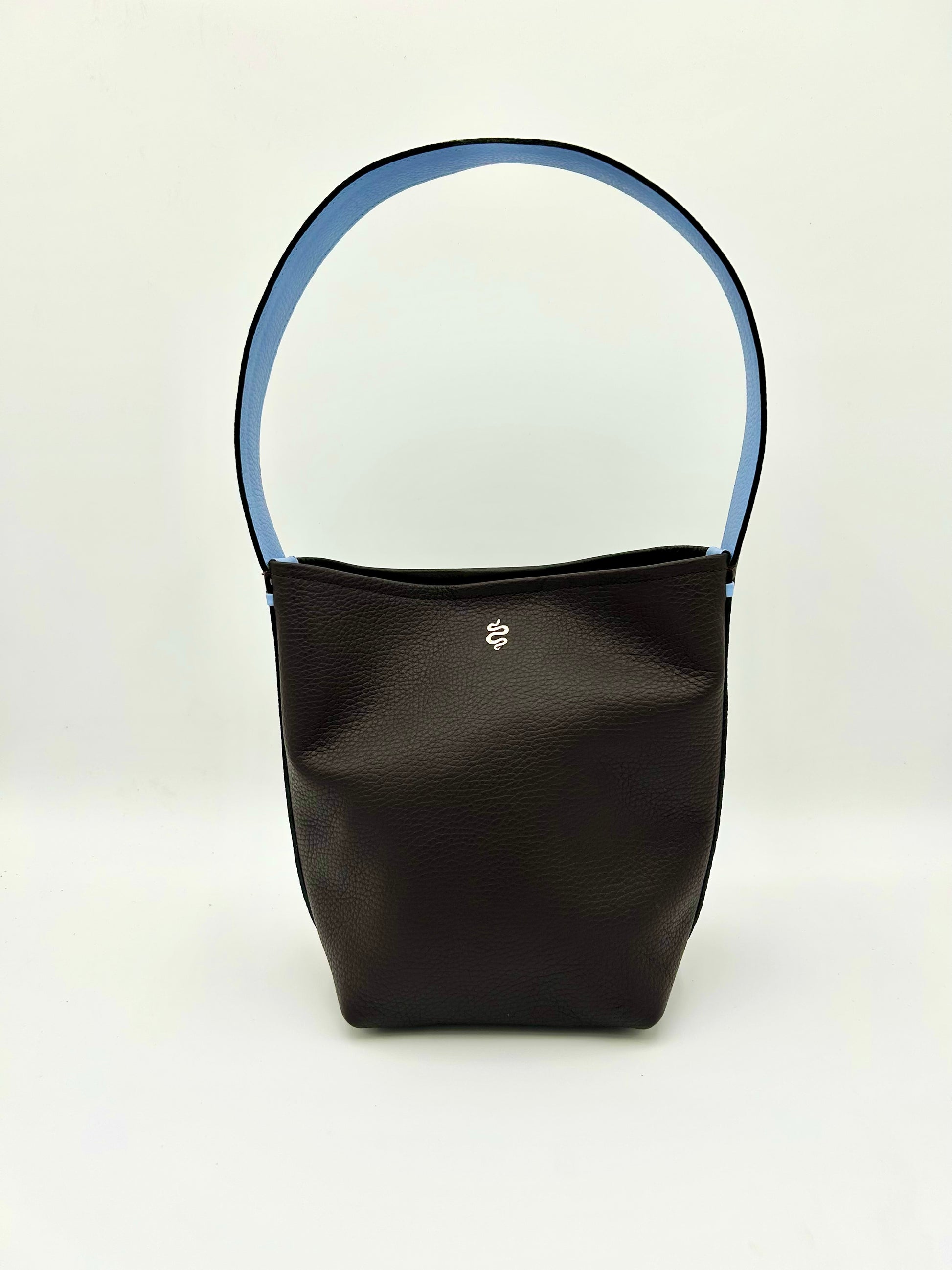 The Grace bucket bag from The Furies Collective in Espresso with Light Blue Underhandle — pebble leather with snap closure and contrasting underhandle.