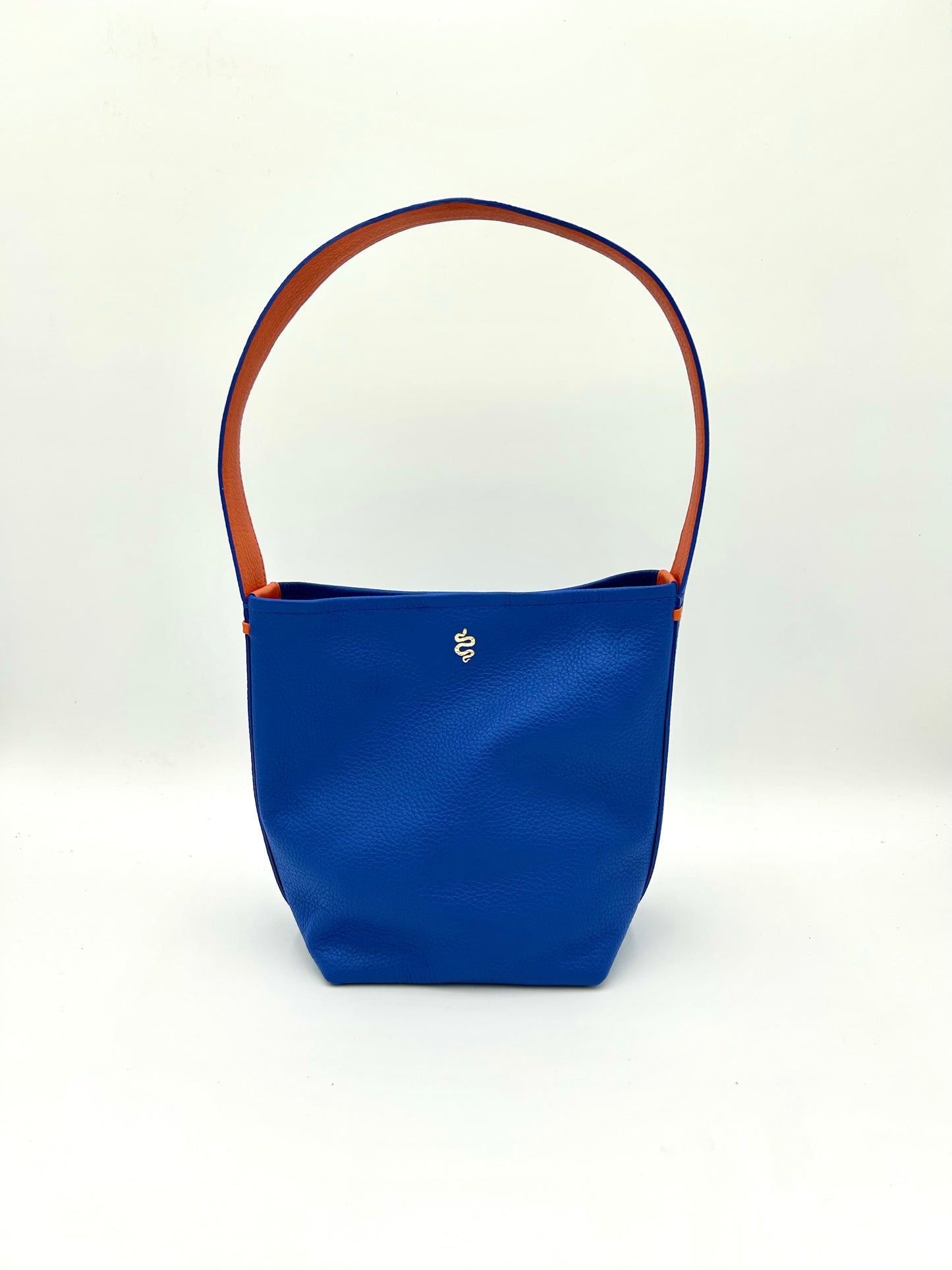 The Grace bucket bag from The Furies Collective in Sapphire with Bright Orange Underhandle — pebble leather with snap closure and contrasting underhandle.