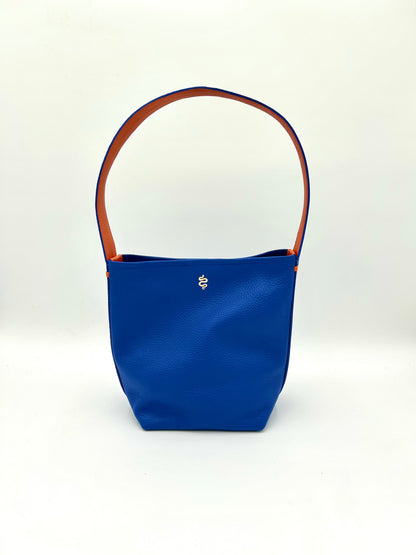 The Grace bucket bag from The Furies Collective in Sapphire with Bright Orange Underhandle — pebble leather with snap closure and contrasting underhandle.