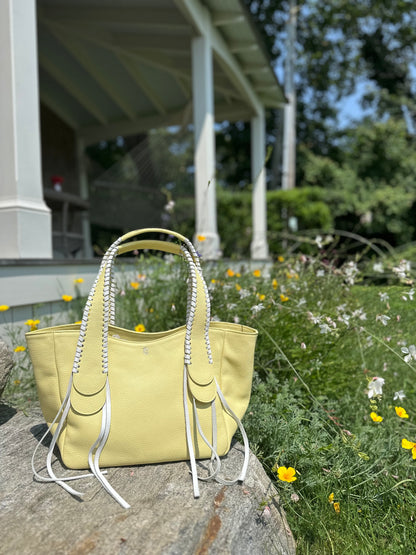 The Talitha tote handbag from The Furies Collective in Canary with lacing in Snow — pebble leather with whipstitched fringe handles and the Furies snake logo.