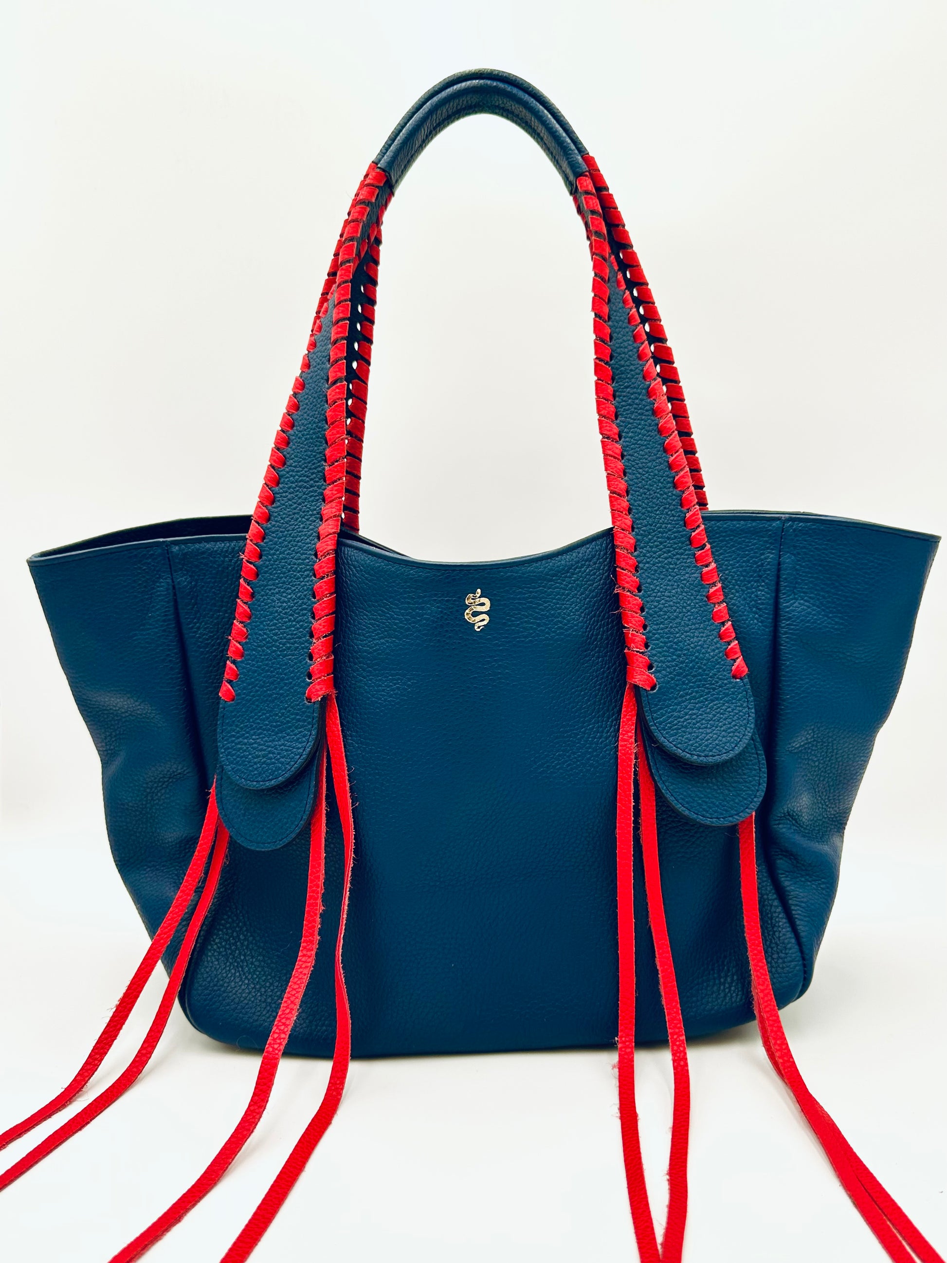 The Talitha tote handbag from The Furies Collective in Navy with Red Lacing — pebble leather with whipstitched fringe handles and the Furies snake logo.
