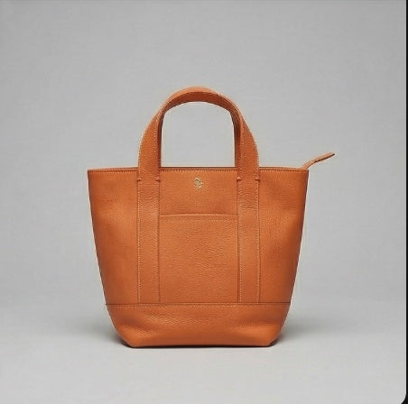 The Small Carolyn crossbody handbag from The Furies Collective in Bright Orange — pebble leather with zip top and exterior pocket.